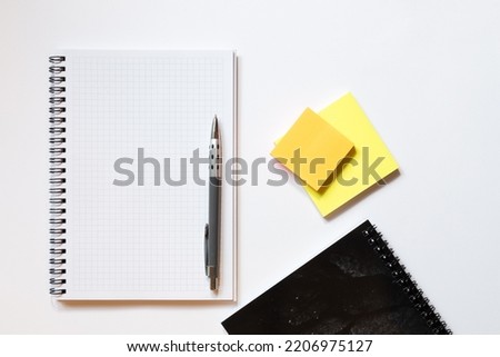 Top down flat lay view of notepad with white pages, pen and sticky note blocks on white background