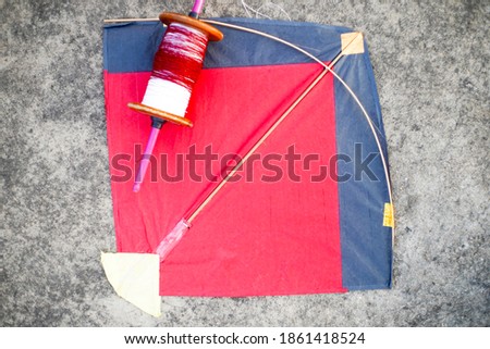 Top down flatlay shot with red and black paper and wood kite with a wooden handmade charkhi thread spool with normal and glass covered thread for kite fighting on teh indian festival of makar