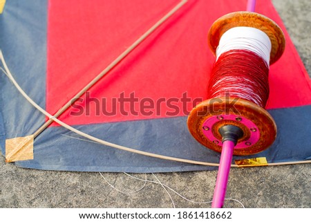 Top down flatlay shot with red and black paper and wood kite with a wooden handmade charkhi thread spool with normal and glass covered thread for kite fighting on teh indian festival of makar