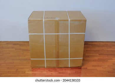 Top Down Front View Of Large Brown Blank Cardboard Box On Wooden Floor, Against White Wall. For Advertising Branding Template Mock Up Purpose. Home Delivery Concept.