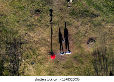 Top Down Nadir View Of Silhouettes Of Couple Holding Hands In The Nature. Beautiful Aerial Drone Shot Of Man And Woman Shadows In Grass Next To Tourist Information Pole, Shadows Of Two People In Grass