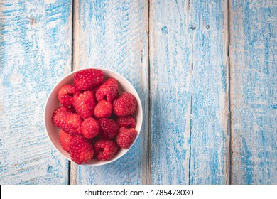 Top Down Overhead Shot Of A White Bowl Filled With Fresh Juicy Raspberries On A Rustic Weathered Worn Light Blue Wood Table Surface