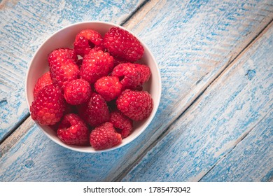 Top Down Overhead Shot Of A White Bowl Filled With Fresh Juicy Raspberries On A Rustic Weathered Worn Light Blue Wood Table Surface