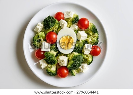 Top down overhead view of a fresh healthy salad with broccoli tomatoes cheese and boiled egg on a white plate isolated on a white background.
