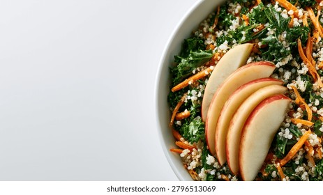 Top down partial view of a fresh healthy kale and quinoa salad bowl with shredded carrots and sliced apples isolated on a white background with copy space.