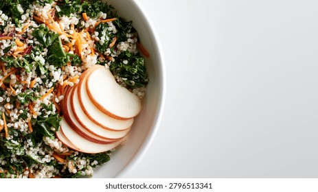 Top down partial view of a fresh healthy kale and quinoa salad with shredded carrots and sliced apples in a white bowl with copy space.