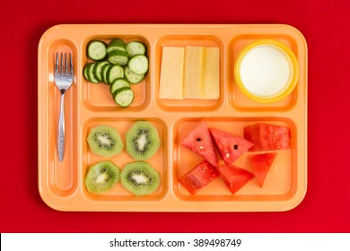 Top Down Perspective View On Bright Plastic Child Size Lunch Tray With Fork, Cucumber, Cheese, Kiwi, Watermelon Slices And Little Cup Of Milk