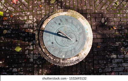 Top Down Photo Of A Stone And Metal Sundial On A Mottled Brick Garden Path