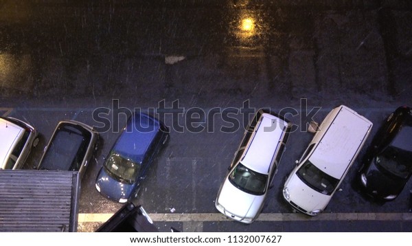 Top down picture of city streets at night and\
heavy rainfall and thunderstorm flashes illuminating the streets\
and parked cars for short period of time typical city scene during\
rain season