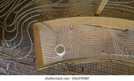 TOP DOWN: A Roll Of Tubing Is Unwinding As Floor Heating Is Laid Across A Modern Wooden House Under Construction. Ground Central Heating Is Being Installed In A Large Housing Project In Progress.