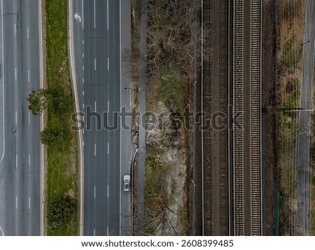 A top down shot directly above train tracks next to an empty Sunrise Highway on Long Island, NY during a cloudy day with no people in view. Shot with a drone camera.