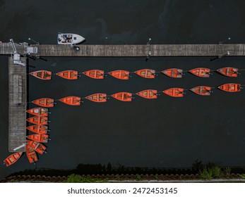 A top down shot over a small fleet of small orange motorboats anchored to a wooden pier in a calm lake on a cloudy day in The Bronx, New York. - Powered by Shutterstock