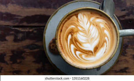 Top down shot of a perfectly made cappuccino made with locally grown coffee with a latte art rosetta on a worn wooden table framed to the right with a blurry background
