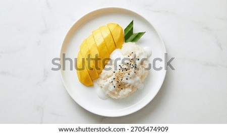 top down shot of Thai mango sticky rice dessert, sliced ripe yellow mango arranged beside glossy coconut sticky rice topped with sesame seeds, on a simple white plate