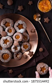 Top Down Vertical View Of Chocolate Linzer Cookies On A Copper Tray With A Hand Holding One Cookie.