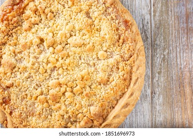 A Top Down View Of An Apple Crumble Pie, On A Wooden Table Surface, Cut Off On The Left Side Of The Frame.