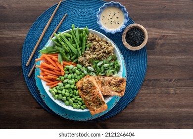 Top Down View Of An Asian Salmon Salad Bowl With Toppings On A Wooden Table.