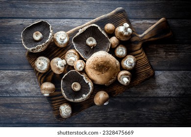 A top down view of assorted portobello and cremini mushrooms on a wooden board.