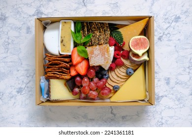 Top down view of assortment of fruits cheeses crackers in a box isolated on marble pattern table background. Concept for food delivery catering or gift for holiday season or packaging mock up. - Powered by Shutterstock