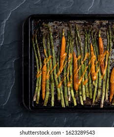 A Top Down View Of A Baking Sheet Of Baked Asparagus And Baby Carrots With Dressing Drizzled On Top.