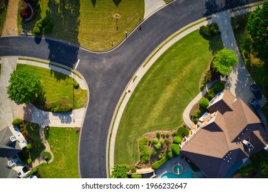 Top down view of beautiful houses, roofs and lush green landscaped yards in an upscale subdivision in suburbs of USA shot during Golden hour during early spring.