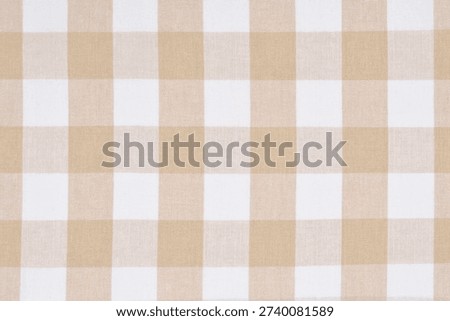A top down view of a beige and white checkered linen fabric with a classic gingham pattern suitable for tablecloths or kitchen textiles