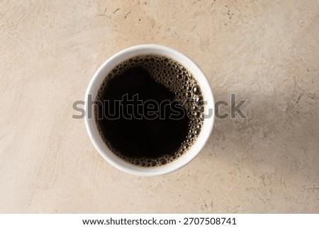 A top down view of a black coffee in a paper cup.