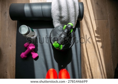 Top down view of black exercise mat featuring adjustable fitness equipment in green and pink alongside a white towel, arranged for a home workout session. The scene highlights indoor fitness, healthy lifestyle habits, and convenient home exercise equipment in a modern domestic setting.