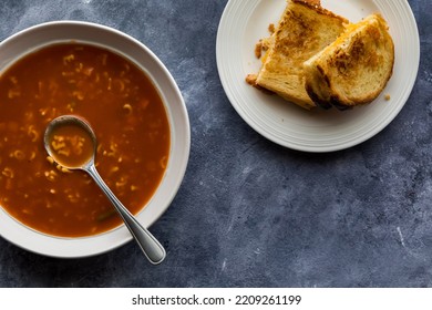 Top Down View Of A Bowl Of Alphabet Soup Served With A Grilled Cheese Sandwich.