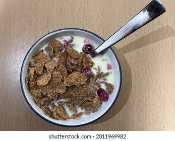 Top Down View Of A Bowl Of Healthy  Cereal With Milk. Bran Cereal With Fruit Pieces Against A Wooden Table For Breakfast.