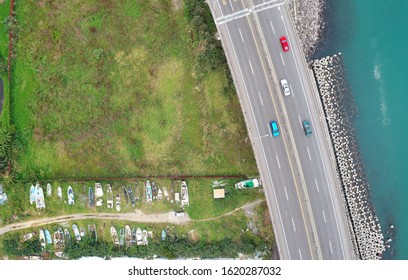 Top down view of cars driving on a coastal highway that is protected with the concrete wave breaker & dismantled fishing boats abandoned on the nearby meadows in Bali District, New Taipei City, Taiwan