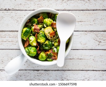 A Top Down View Of A Casserole Dish Filled With Cooked Brussel Sprouts And Bacon And Lemon Cream Sauce With A White Spatula For Serving.