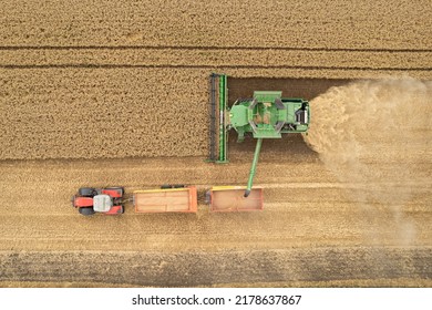 Top Down View Of Combine Harvester On Wheat Field And Unloading To Tractor Trailer.