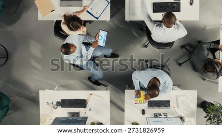 Top down view of corporate workers assessing business objectives and targets. Charts, diagrams and reports highlight progress and business intel for market research.
