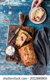 Top Down View Of A Cranberry Rosemary Loaf With A Hand Holding A Plate With One Slice, Ready For Eating.