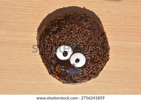 Top down view of a creative chocolate donut featuring edible candy eyes and chocolate vermicelli sprinkles on light wood