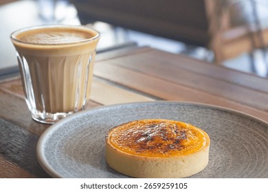Top down view of a custard pudding tart on plate and a cup of cappuccino. Tin Hau, Hong Kong
