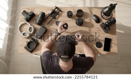 Top down view of desktop where videographer clean dust and dirt from equipment. man in cap work with lens from photo camera or video camera. photographer takes care of equipment. Lens repair service.