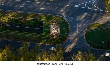 A Top Down View Directly Above Power Lines, A Tower, Road And Greenery In A Suburban Neighborhood On A Sunny Day.