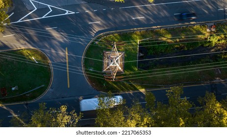 A Top Down View Directly Above Power Lines, A Tower, Road And Greenery In A Suburban Neighborhood On A Sunny Day.