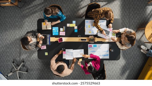 Top Down View: Diverse and Creative Colleagues Working Together at The Conference Table In Stylish Office. Male and Female Business People Using Tablets, and Laptops to Analyze Business Data on Charts