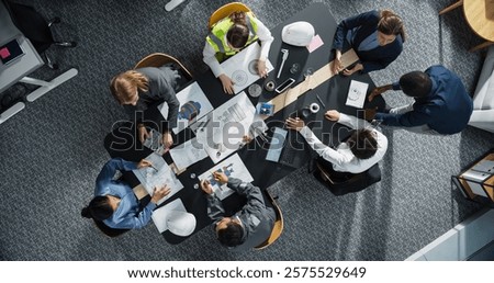 Top Down View of Diverse Team of Real Estate Construction Engineers Discussing Blueprints, Documents in Corporate Office. Modern Workspace of Architectural Bureau With Colleagues Using Tablet, Laptop.
