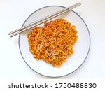 Top down view of dry (no soup) spicy Korean instant noodles with chopsticks on plate, against white background. Samyang ramen noodles topped with sesame and seaweed