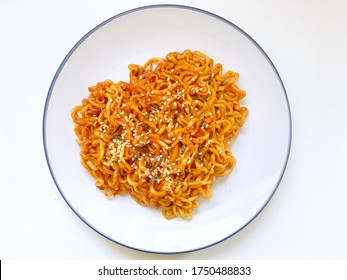 Top down view of dry (no soup) spicy Korean instant noodles against white background. Samyang ramen noodles topped with sesame and seaweed
