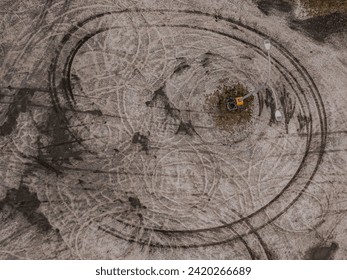 A top down view of an empty sandlot with vehicle skid marks and tire track patterns, taken on a cloudy day.