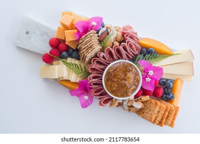 Top down view of a fancy tropical charcuterie cheese board platter with a variety of fruits, meat, cheese, crackers, dip, and flowers. Isolated against a white background. - Shutterstock ID 2117783654