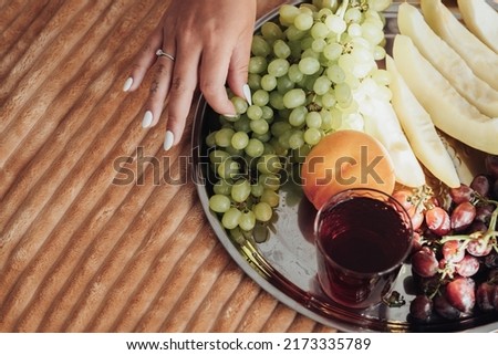 Top Down View of Female Hand Picking Grapes from Tray of Fruit That Lies on Bed