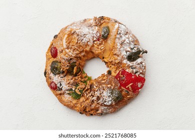 A top down view of a festive wreath shaped cake decorated with candied fruit and nuts on a white plate