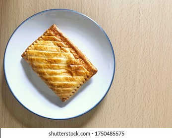 Top down view of flakey golden brown baked pasty on white plate on wooden table - Shutterstock ID 1750485575