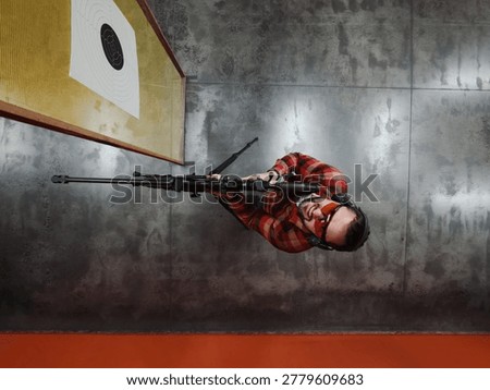 Top Down View of a Focused Marksman with Precision Sniper Rifle and Optical Sight Standing at Indoor Shooting Range.